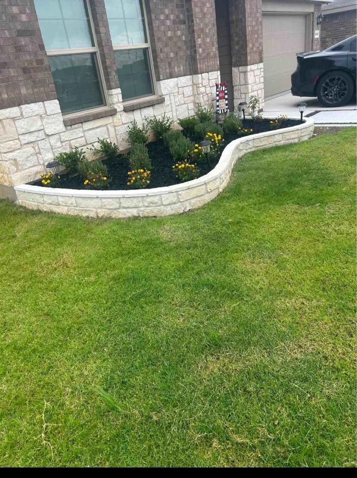 Curved stone border with fresh mulch, shrubs and seasonal flowers